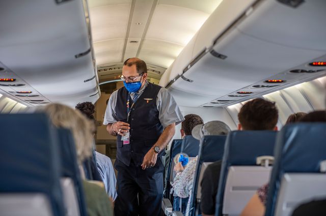 A flight attendant wearing a face mask makes his way down the aisle of a United airlines flight.